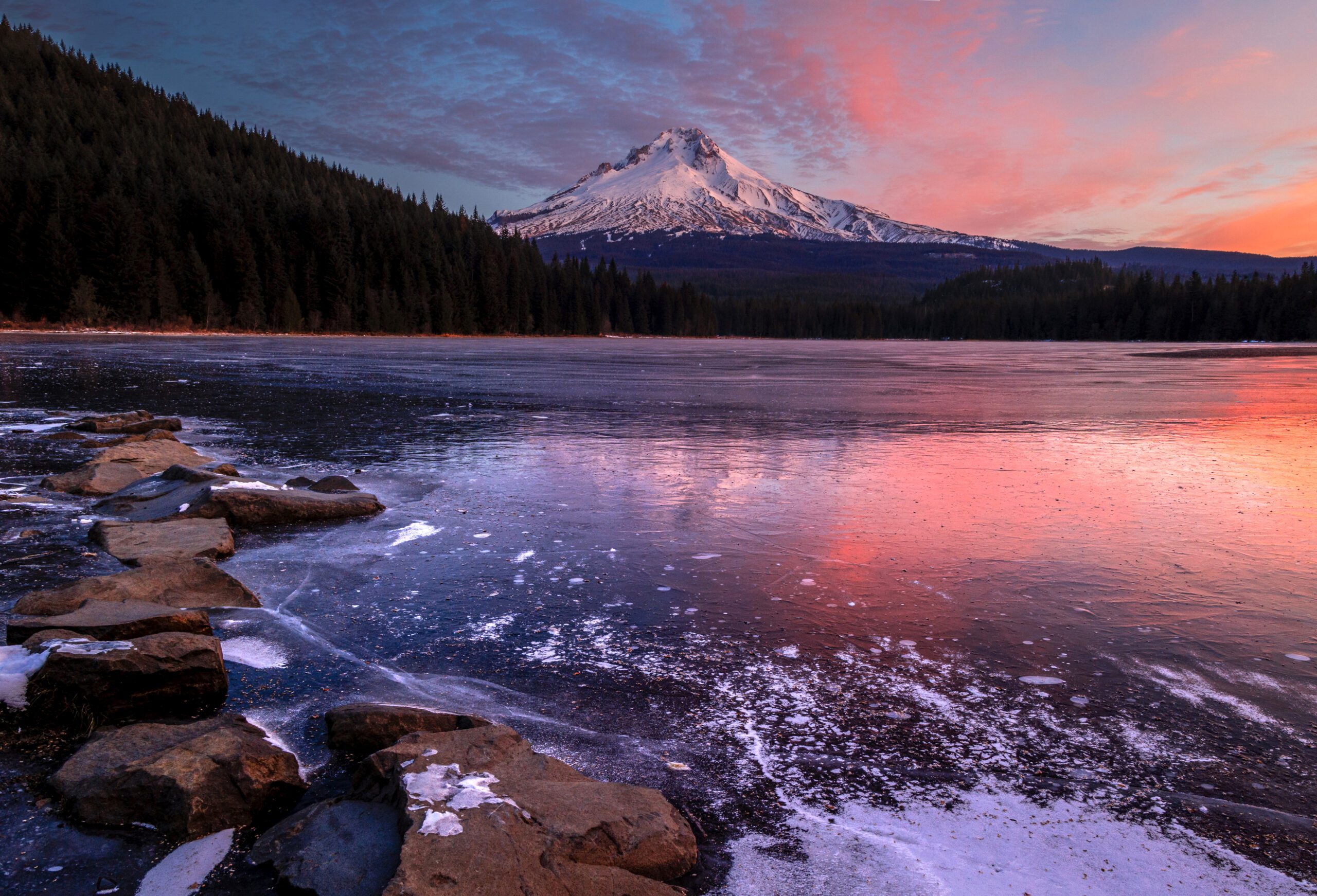 Brilliant oranges, reds and pinks streak through the sky over mount hood, with the colors reflected in a lake